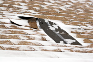 Damaged roof shingles blown off during a windy winter storm.